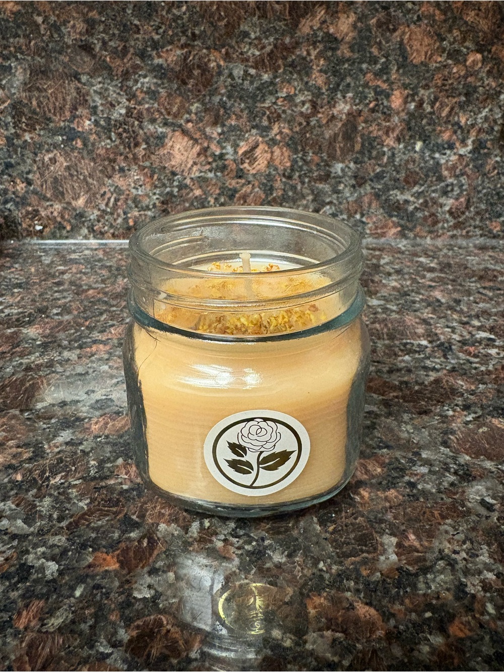 Handmade candle rose scented poured in a jar with yellow flower petals on top